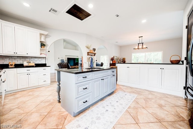 kitchen featuring pendant lighting, a center island with sink, white cabinets, backsplash, and sink