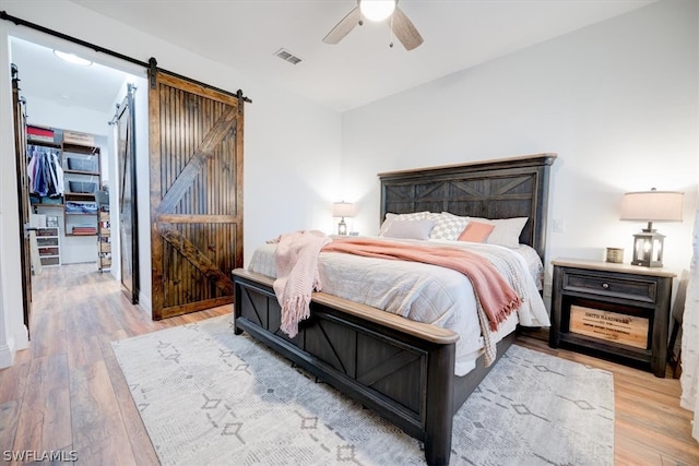 bedroom with a barn door, ceiling fan, and light wood-type flooring