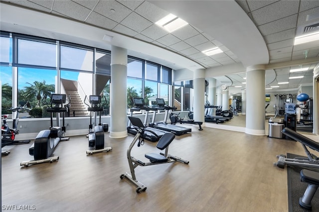 workout area featuring wood finished floors, a paneled ceiling, and ornate columns