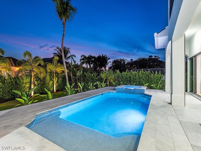 pool at dusk featuring a patio area and an in ground hot tub