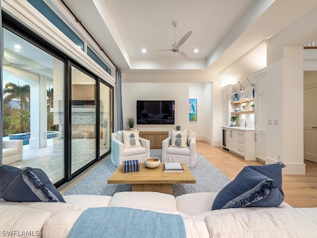 living room featuring a raised ceiling, ceiling fan, and light hardwood / wood-style flooring