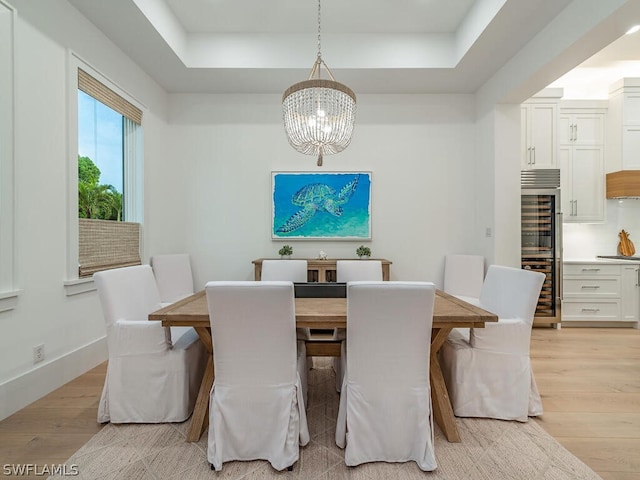 dining space with a tray ceiling, light hardwood / wood-style floors, and a notable chandelier