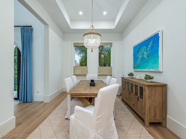 dining room featuring an inviting chandelier, a raised ceiling, and light wood-type flooring