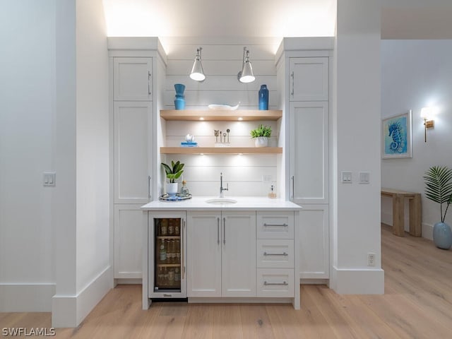 bar featuring tasteful backsplash, sink, white cabinets, beverage cooler, and light wood-type flooring