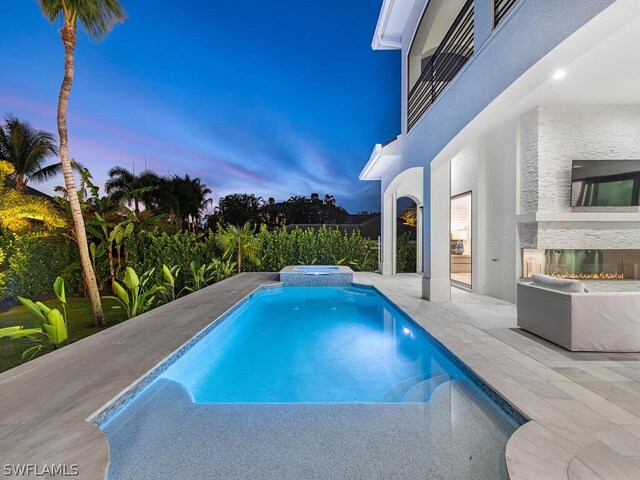 pool at dusk featuring an in ground hot tub and a patio area