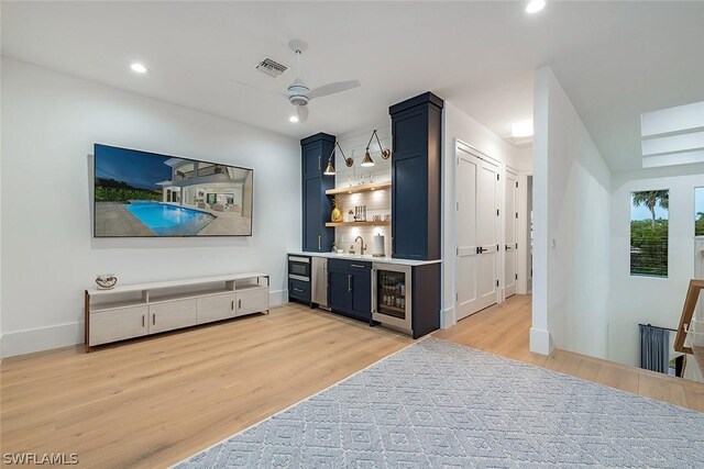 bar with wine cooler, ceiling fan, blue cabinets, and light hardwood / wood-style floors