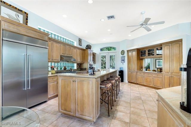 kitchen with stainless steel built in fridge, light tile patterned flooring, a kitchen island, a kitchen bar, and light stone countertops