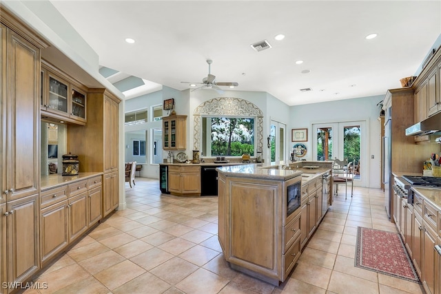 kitchen with appliances with stainless steel finishes, ceiling fan, light tile patterned floors, an island with sink, and french doors