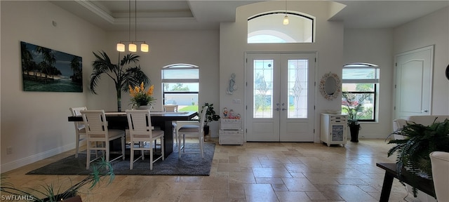 tiled entryway with a high ceiling, a tray ceiling, french doors, and a healthy amount of sunlight