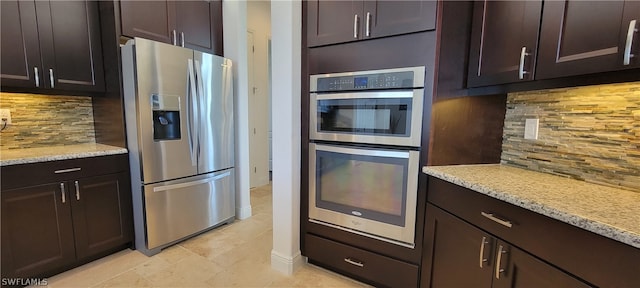 kitchen featuring light tile floors, light stone counters, appliances with stainless steel finishes, tasteful backsplash, and dark brown cabinetry