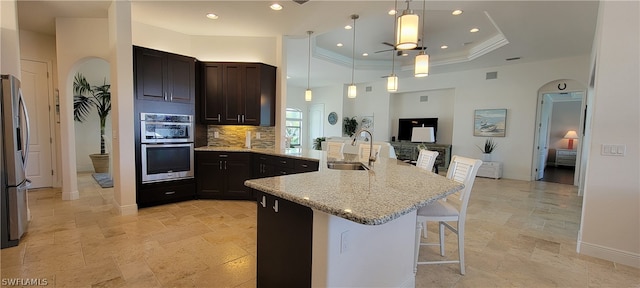 kitchen with backsplash, ceiling fan, a kitchen breakfast bar, sink, and a raised ceiling