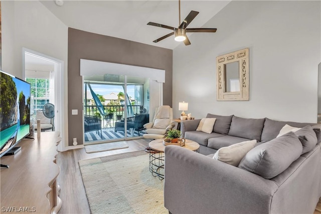 living area with light wood-type flooring, high vaulted ceiling, a ceiling fan, and baseboards