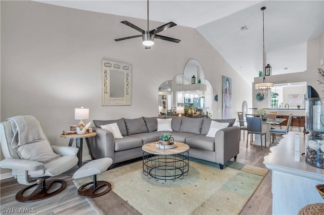 living room with ceiling fan, visible vents, high vaulted ceiling, arched walkways, and wood finished floors