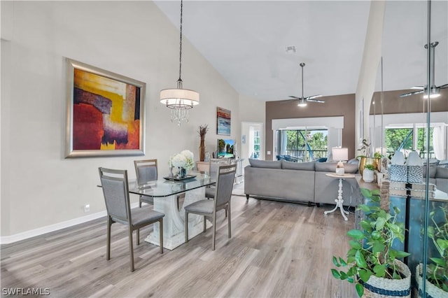 dining area with wood finished floors, baseboards, visible vents, ceiling fan with notable chandelier, and high vaulted ceiling