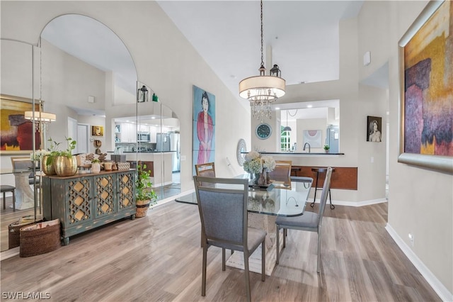 dining room with baseboards, an inviting chandelier, arched walkways, light wood-type flooring, and high vaulted ceiling