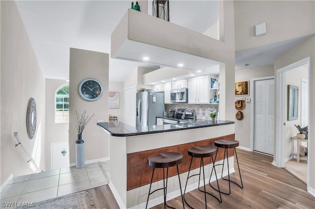 kitchen with white cabinetry, appliances with stainless steel finishes, a kitchen breakfast bar, kitchen peninsula, and backsplash