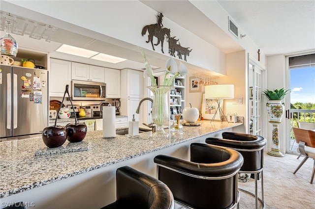 kitchen with a breakfast bar, fridge, white cabinetry, light stone counters, and light colored carpet