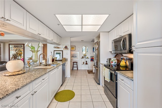 kitchen with appliances with stainless steel finishes, light tile patterned flooring, white cabinetry, a sink, and light stone countertops