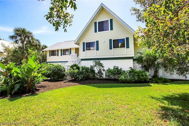 rear view of house with stucco siding, stairs, and a yard