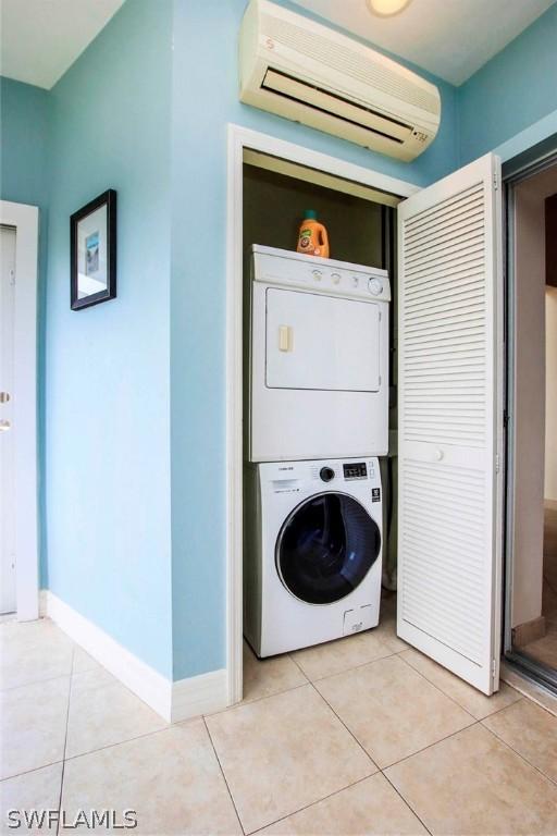 clothes washing area with light tile patterned floors, baseboards, a wall mounted AC, laundry area, and stacked washer / drying machine