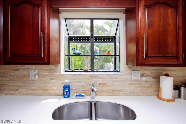 kitchen with a sink, reddish brown cabinets, backsplash, and light countertops