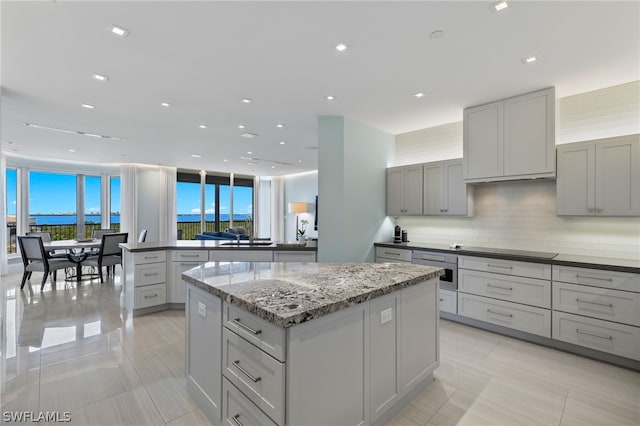 kitchen with light tile patterned floors, gray cabinetry, a center island, tasteful backsplash, and light stone countertops