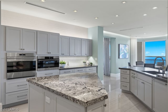 kitchen with sink, a center island, stainless steel oven, and gray cabinetry