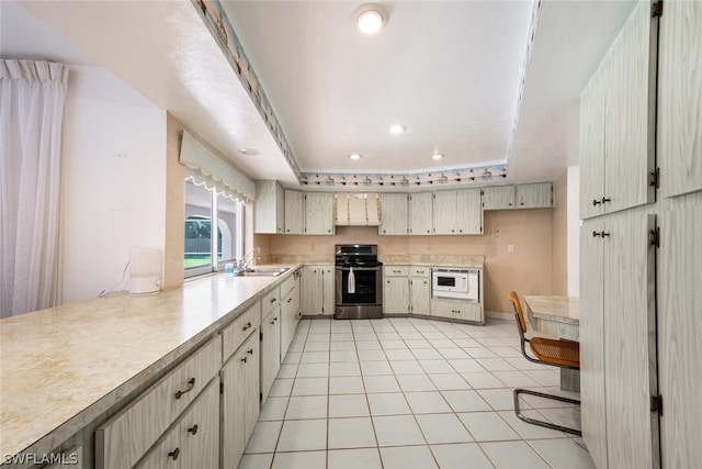 kitchen featuring a tray ceiling, light tile flooring, sink, white microwave, and stainless steel electric range