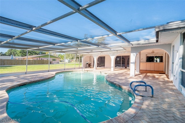 view of swimming pool with a yard, ceiling fan, glass enclosure, and a patio