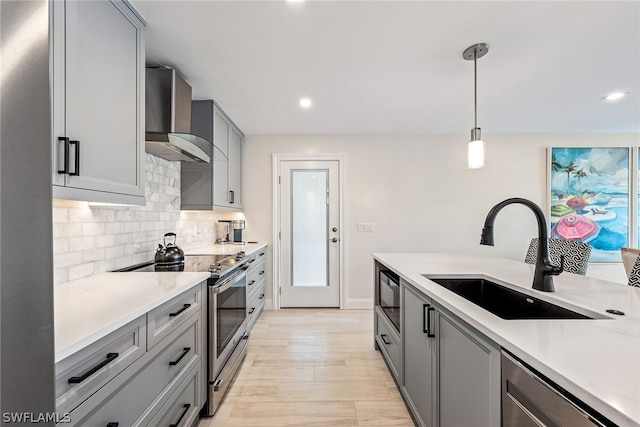 kitchen with sink, gray cabinets, hanging light fixtures, appliances with stainless steel finishes, and wall chimney exhaust hood