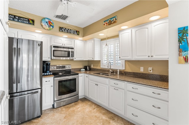 kitchen with ceiling fan, sink, white cabinetry, stainless steel appliances, and dark stone counters