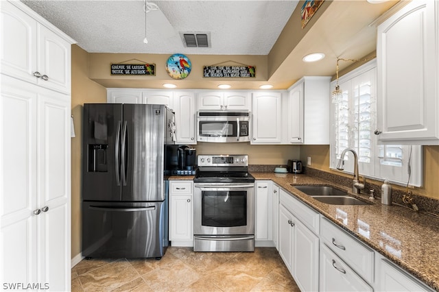 kitchen featuring white cabinetry, appliances with stainless steel finishes, dark stone counters, a textured ceiling, and sink