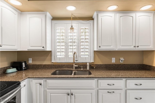 kitchen featuring dark stone countertops, white cabinetry, a sink, and recessed lighting