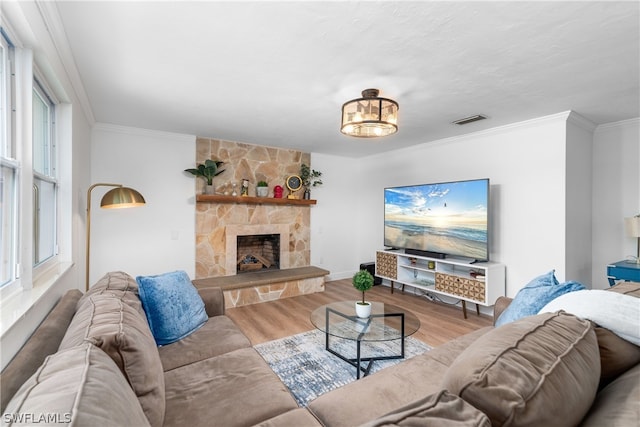 living room featuring a stone fireplace, wood finished floors, visible vents, and crown molding