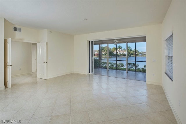 tiled empty room featuring ceiling fan and a water view