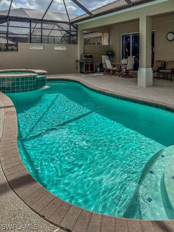 view of swimming pool with an in ground hot tub, a patio area, a lanai, and a grill