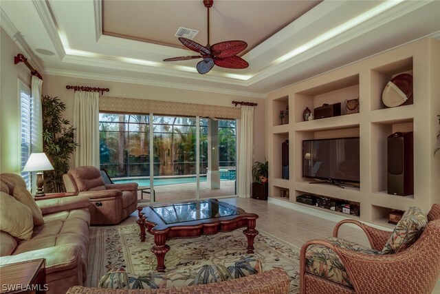 tiled living room featuring ceiling fan, built in features, a tray ceiling, and ornamental molding