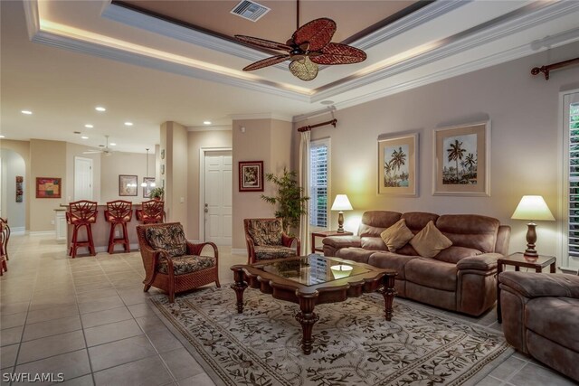 living room featuring crown molding, light tile patterned flooring, a tray ceiling, and ceiling fan