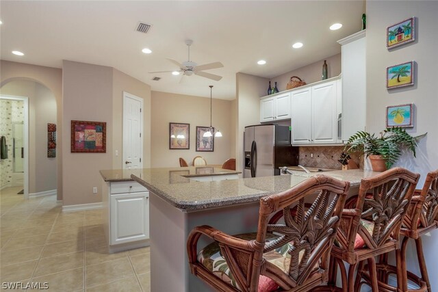 kitchen featuring a kitchen island, backsplash, stainless steel fridge, white cabinets, and light stone counters