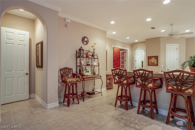 tiled dining room featuring crown molding, indoor bar, and ceiling fan