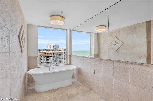 bathroom with tile flooring, a bathtub, a water view, and tile walls