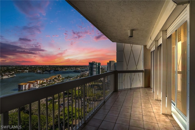 balcony at dusk featuring a water view