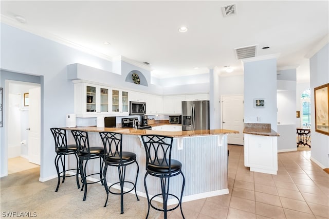 kitchen with white cabinets, appliances with stainless steel finishes, a breakfast bar area, and light tile flooring