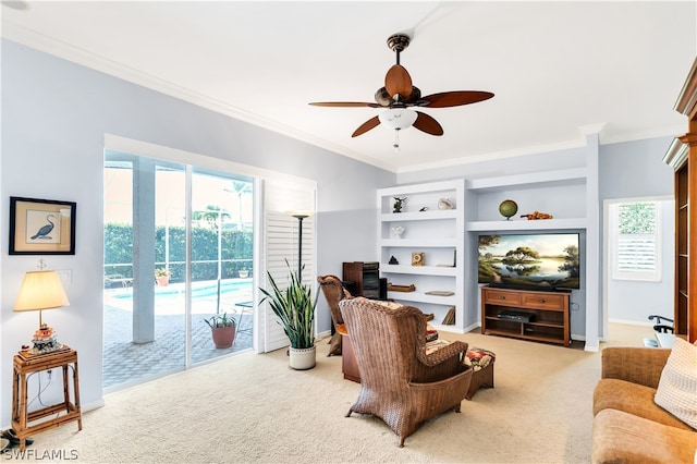 carpeted living room featuring built in shelves, ceiling fan, and crown molding