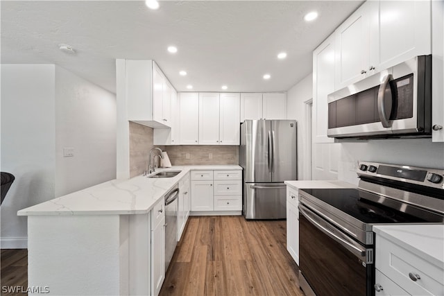 kitchen with appliances with stainless steel finishes, sink, white cabinets, light wood-type flooring, and light stone counters