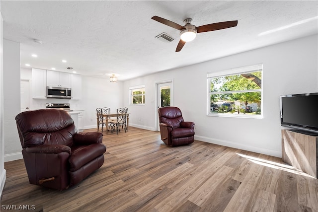 living room with a textured ceiling, ceiling fan, and light wood-type flooring