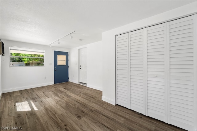 interior space with a textured ceiling, rail lighting, and dark hardwood / wood-style floors