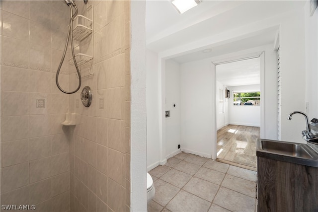 bathroom with toilet, a tile shower, sink, and tile flooring