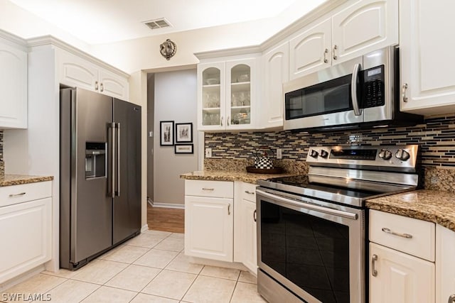 kitchen with light stone counters, light tile patterned floors, stainless steel appliances, decorative backsplash, and white cabinets