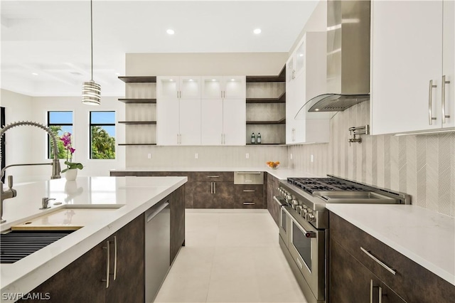 kitchen with wall chimney range hood, appliances with stainless steel finishes, backsplash, white cabinets, and decorative light fixtures